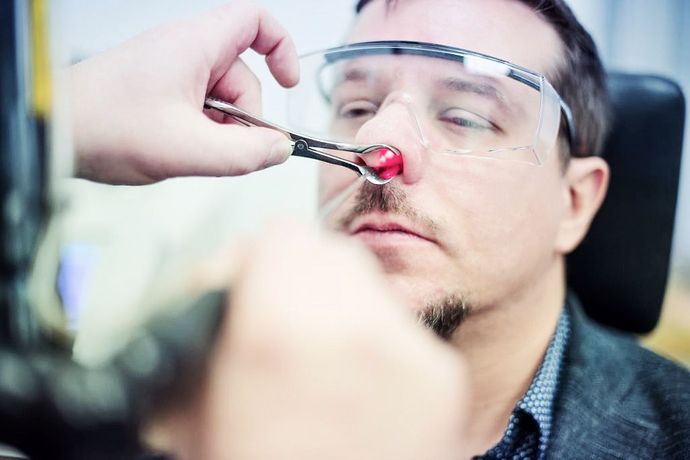 Ein Mann mit Schutzbrille bekommt eine Schraube in die Nase.