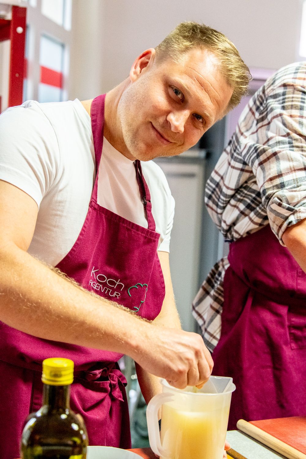 Ein Mann mit einer weinroten Schürze presst in einer Küchenumgebung Zitrusfrüchte in einen Messbecher.