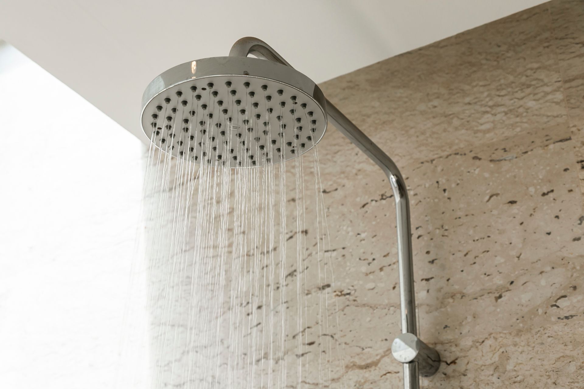 De l'eau sortant d'une colonne de douche installée sur un mur en pierre beige.