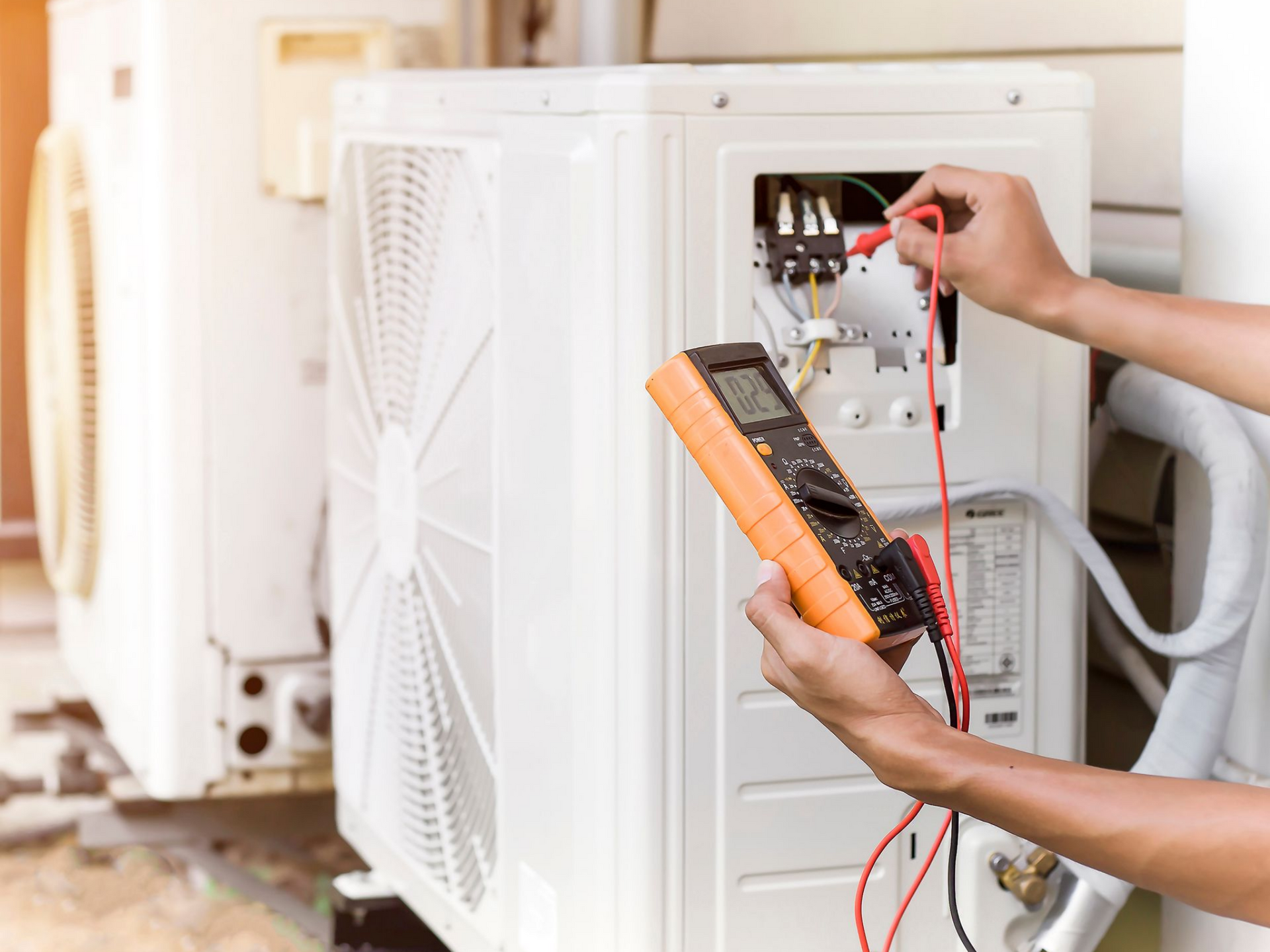 Une personne utilise un multimètre pour inspecter une unité de pompe à chaleur.
