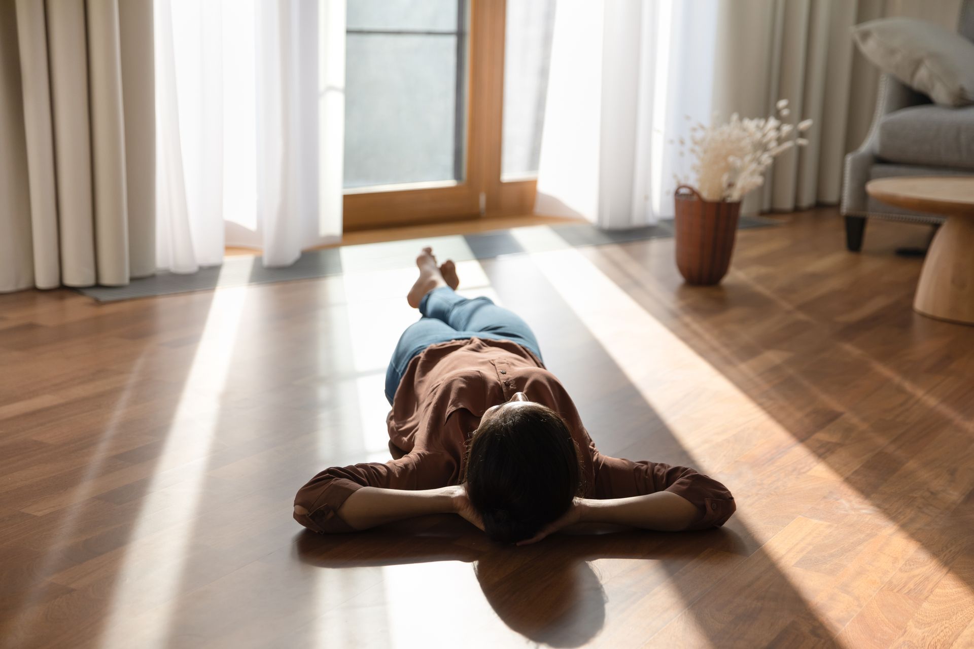Une femme allongée sur le dos sur du parquet, baigné de lumière.