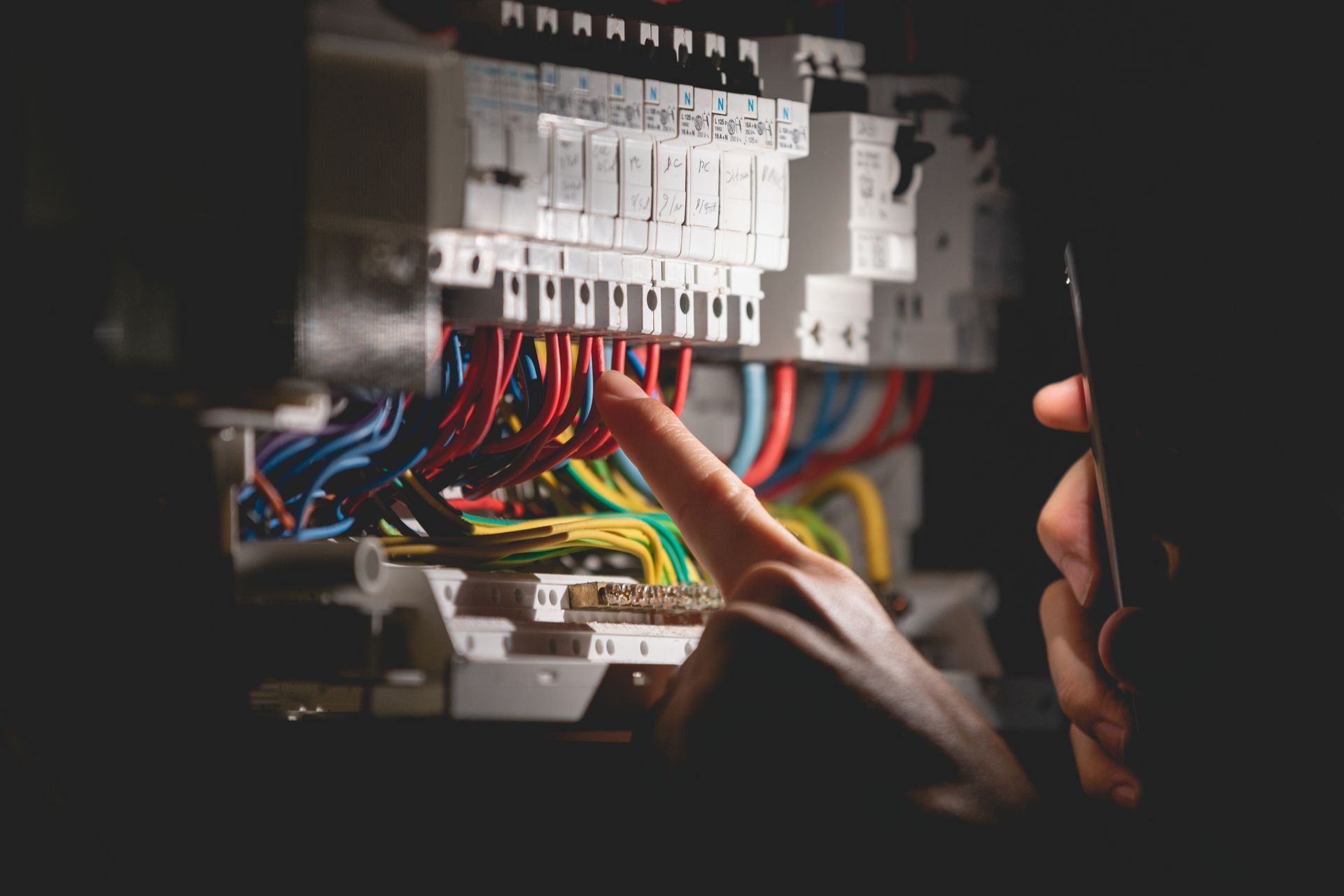 Une personne désigne du doigt des fils électriques sur un tableau électrique.