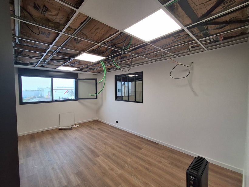 Un espace vide en construction, avec un sol imitation bois, des murs blancs et un plafond inachevé.