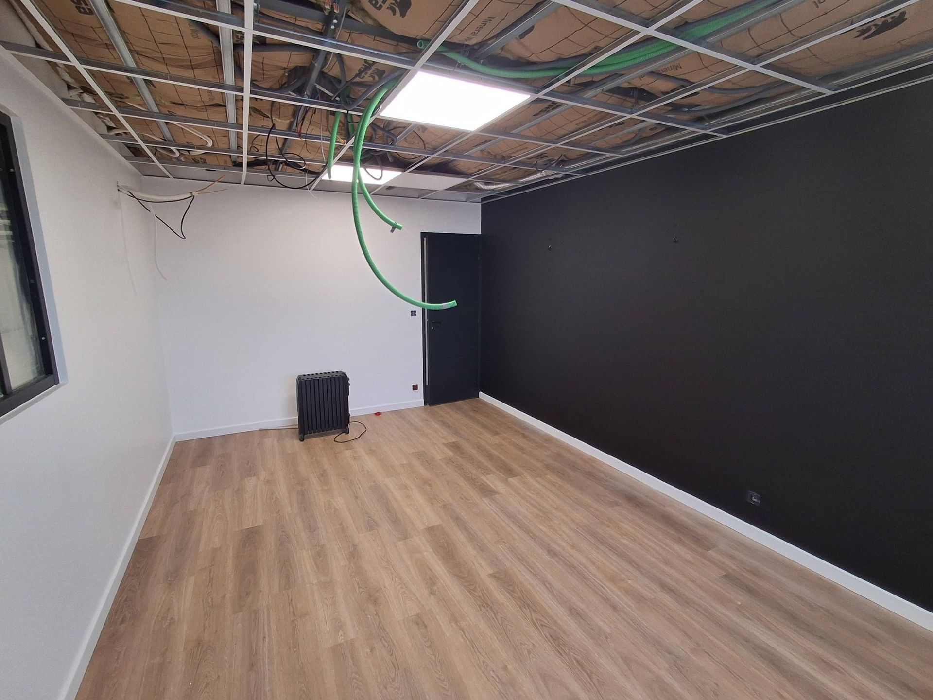 Une pièce en construction avec un sol imitation bois, des murs blancs et noirs, un plafond ouvert.
