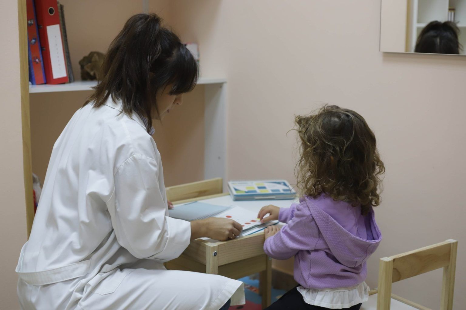 Adulto y niño jugando con juguetes en una pequeña mesa en el interior.