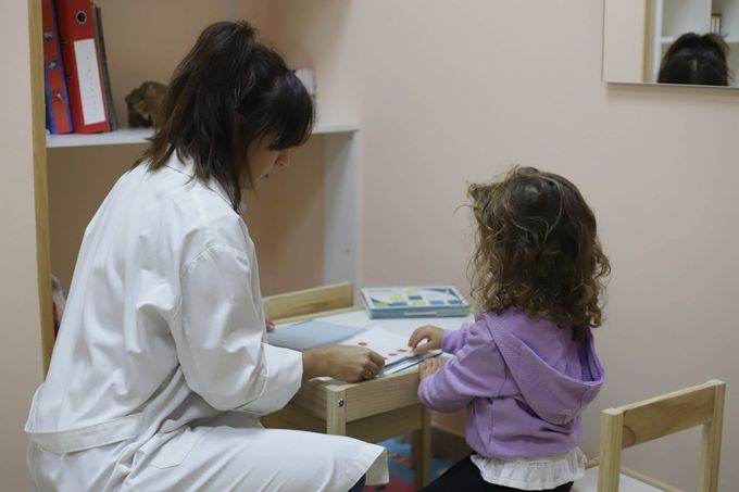 Adulto y niño jugando con juguetes en una pequeña mesa en el interior.
