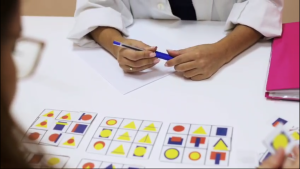 Persona que sostiene un bolígrafo sobre un papel, mirando tarjetas con formas y colores durante una prueba.