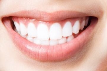 Primer plano de una boca con dientes blancos brillantes y labios rosados ​​en una expresión sonriente.