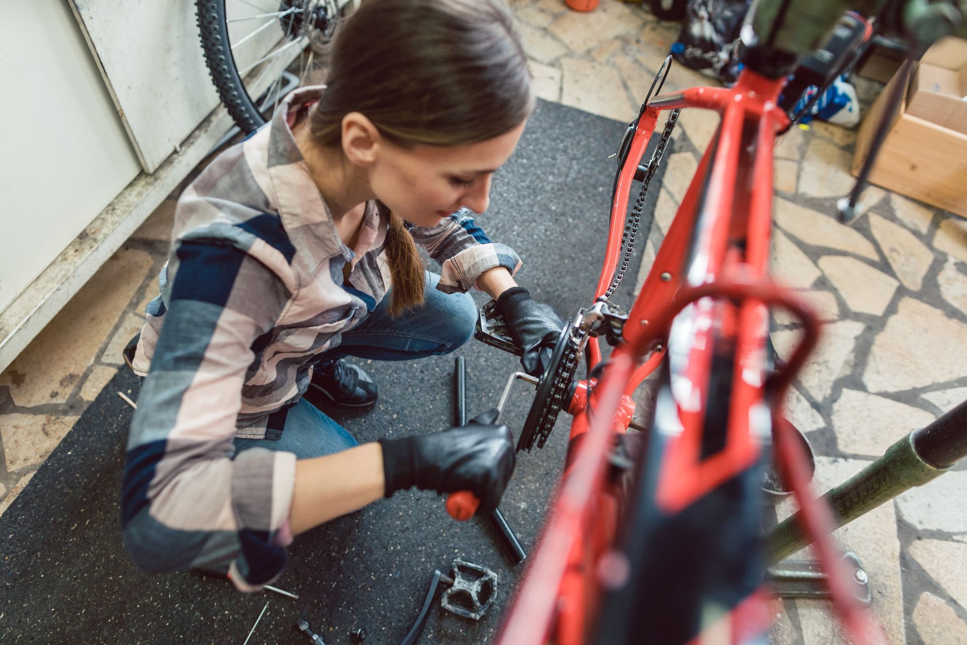 Mujer con guantes trabajando en una bicicleta roja en un taller; está usando una herramienta para ajustar la cadena.