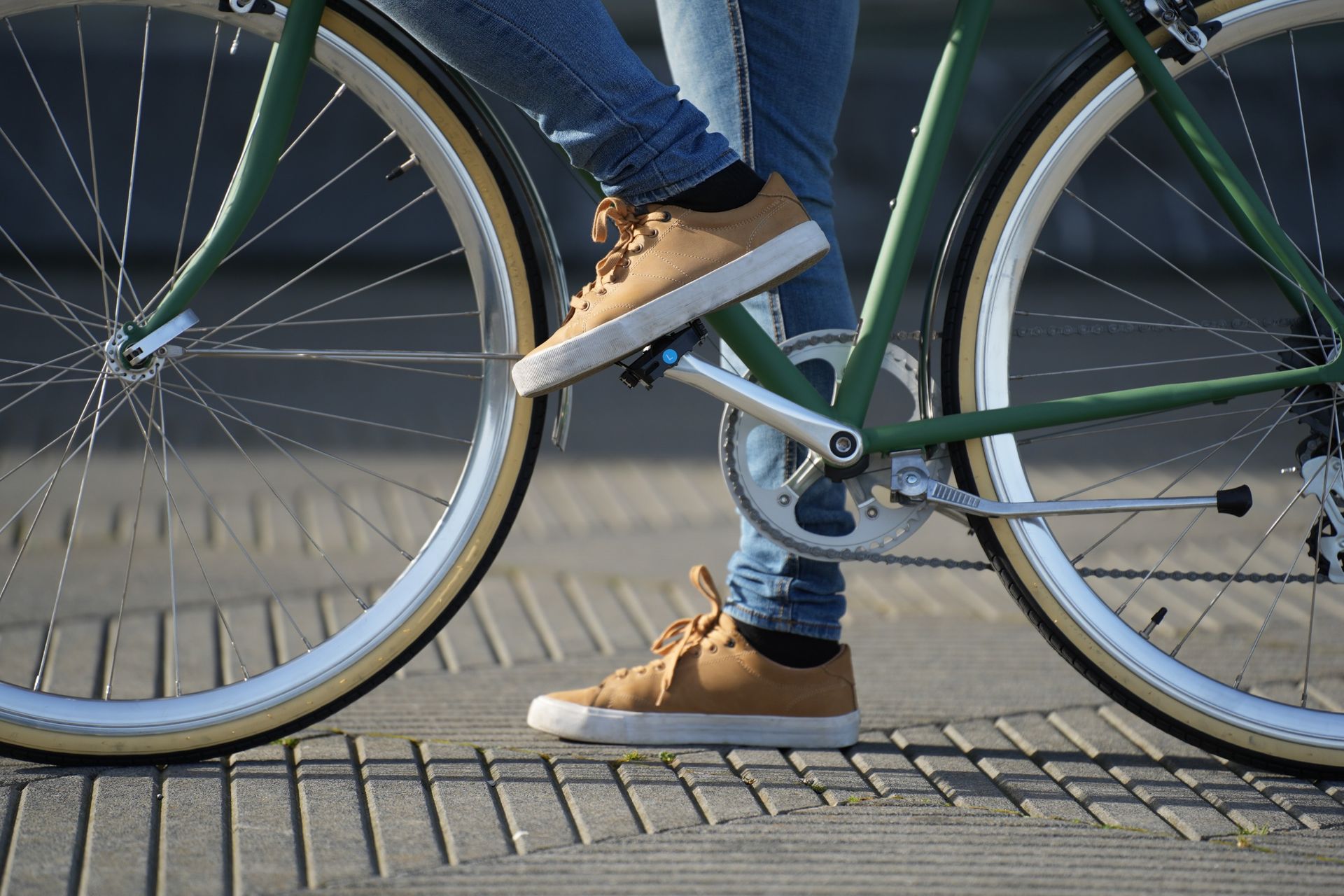 Pies de una persona con zapatillas deportivas sobre pedales de bicicleta. Un pie está en alto. Cuadro de bicicleta verde, al aire libre.