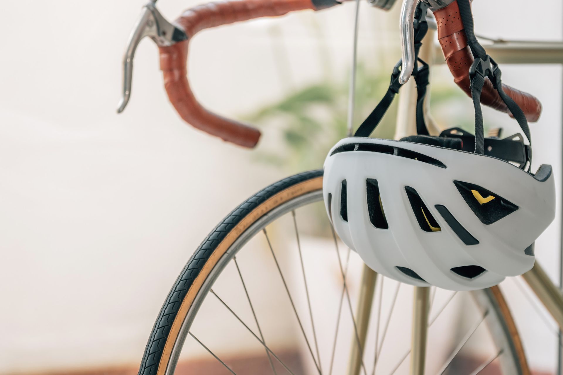 Casco de bicicleta blanco colgado en el manillar de una bicicleta con manillar y llanta de color marrón.