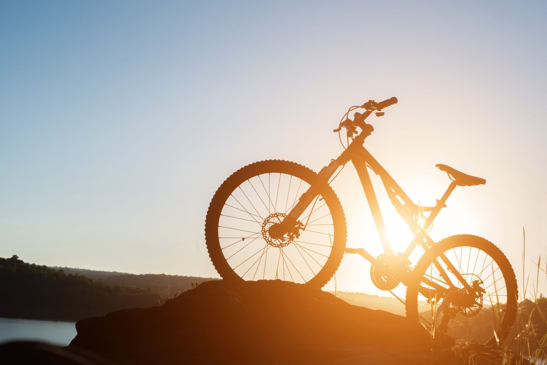 Silueta de bicicleta de montaña contra una puesta de sol sobre un lago.