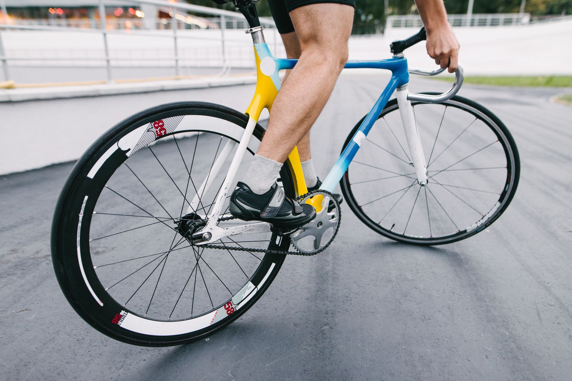 Ciclista en una bicicleta de pista, con zapatillas deportivas, en un velódromo. La bicicleta es azul y amarilla.