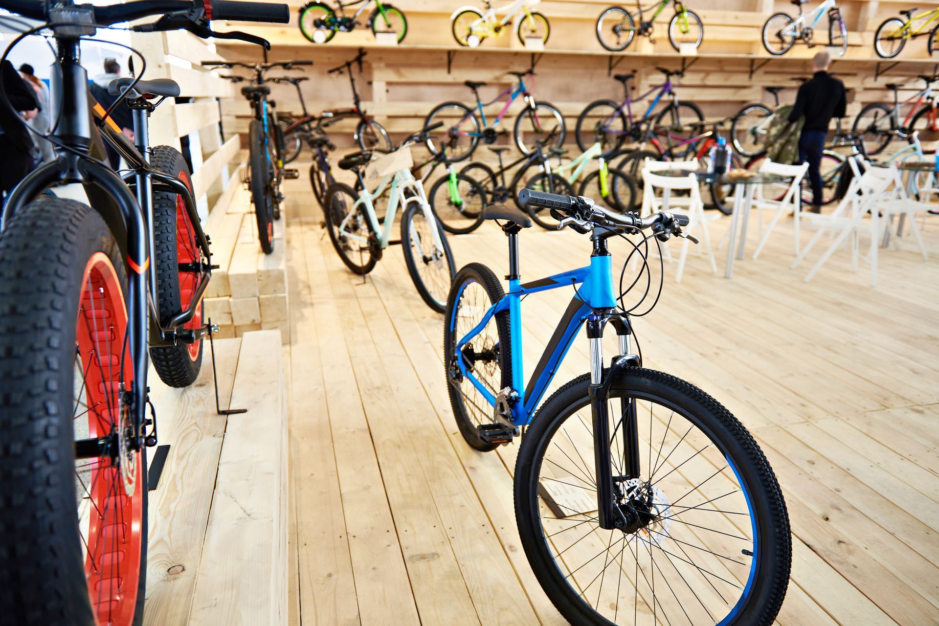 Bicicletas expuestas en una tienda de bicicletas bien iluminada con suelo de madera. Se ven varias personas.
