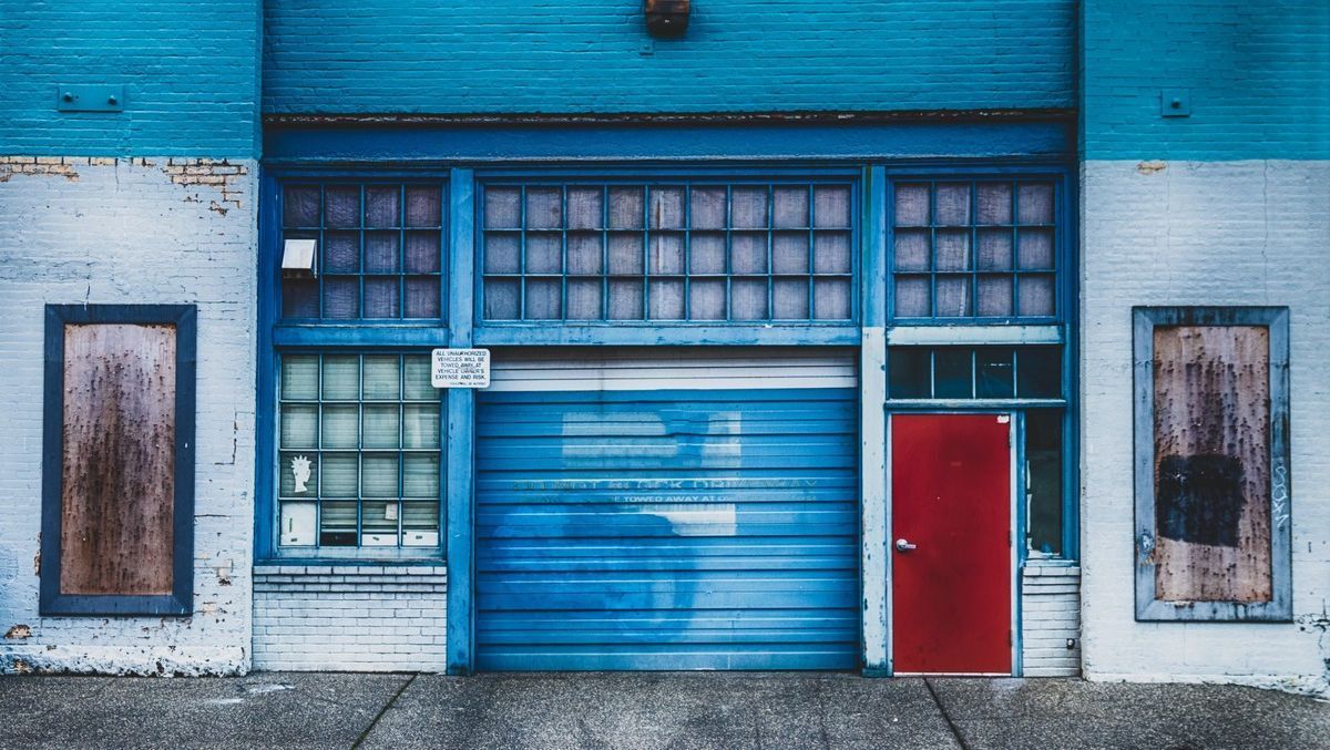 Un edificio azul con una puerta roja y una puerta de garaje azul.