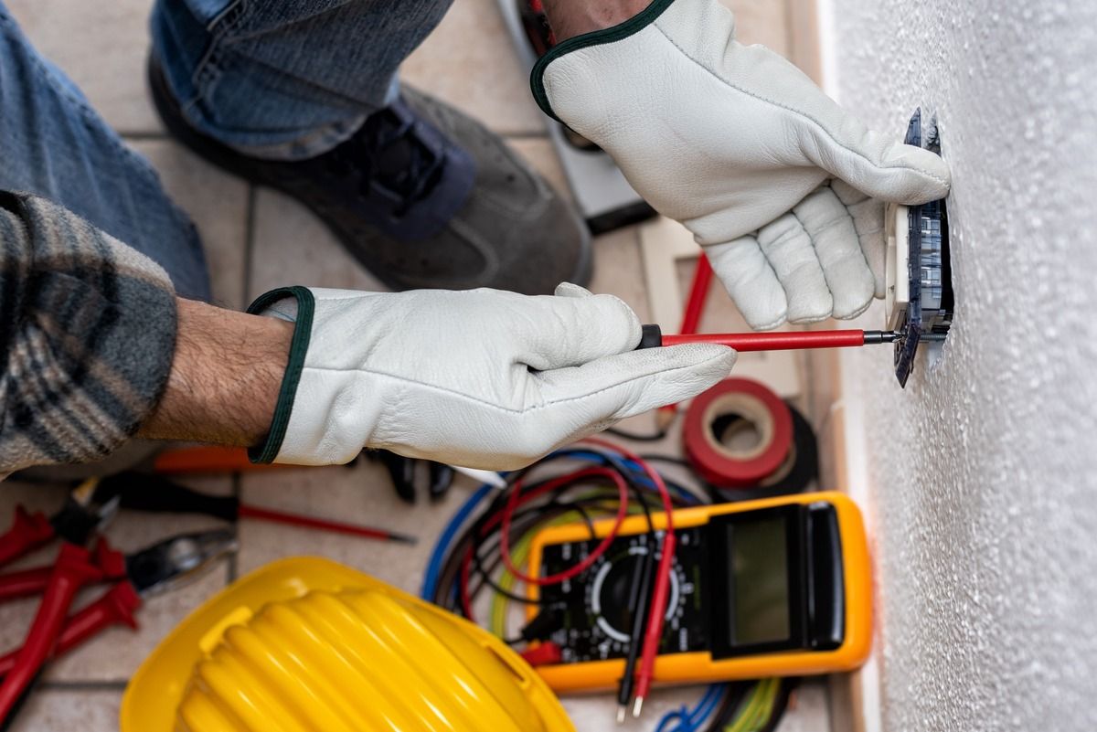 Un hombre está trabajando en una toma de corriente eléctrica con un destornillador.