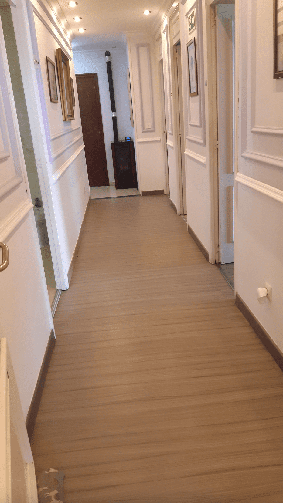 Un largo pasillo con suelo de madera y paredes blancas.