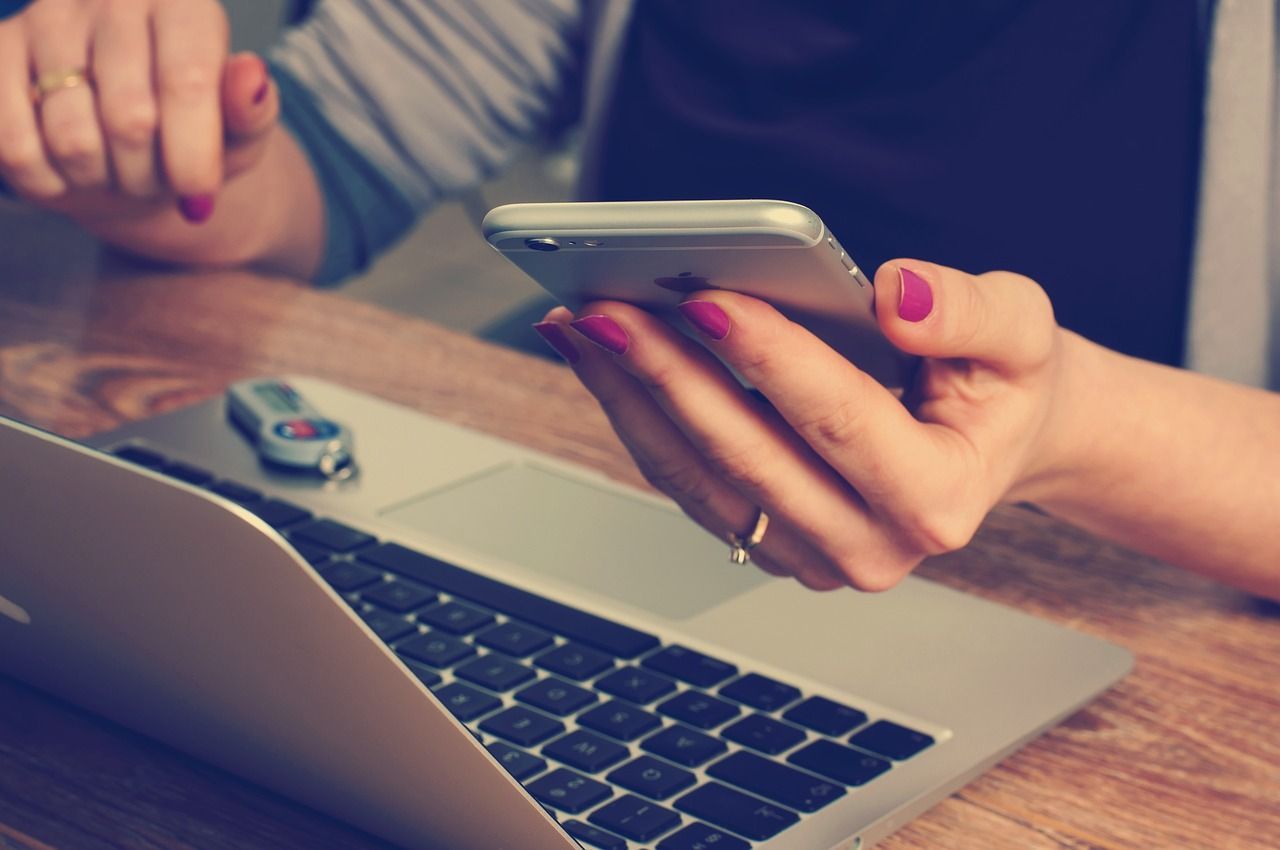 Una mujer sostiene un teléfono celular frente a una computadora portátil.