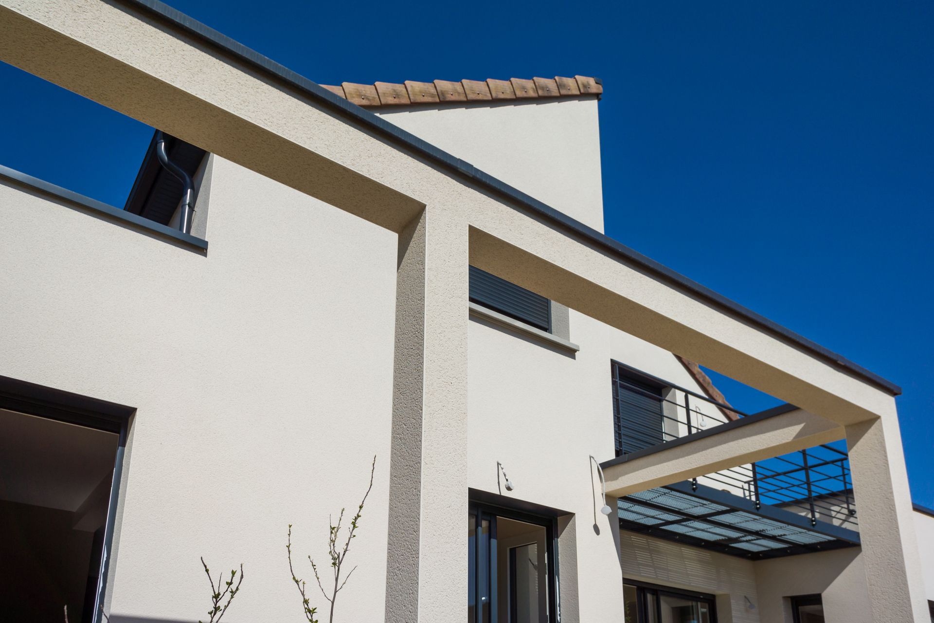 Maison blanche moderne avec toit plat, porche ouvert et ciel bleu.