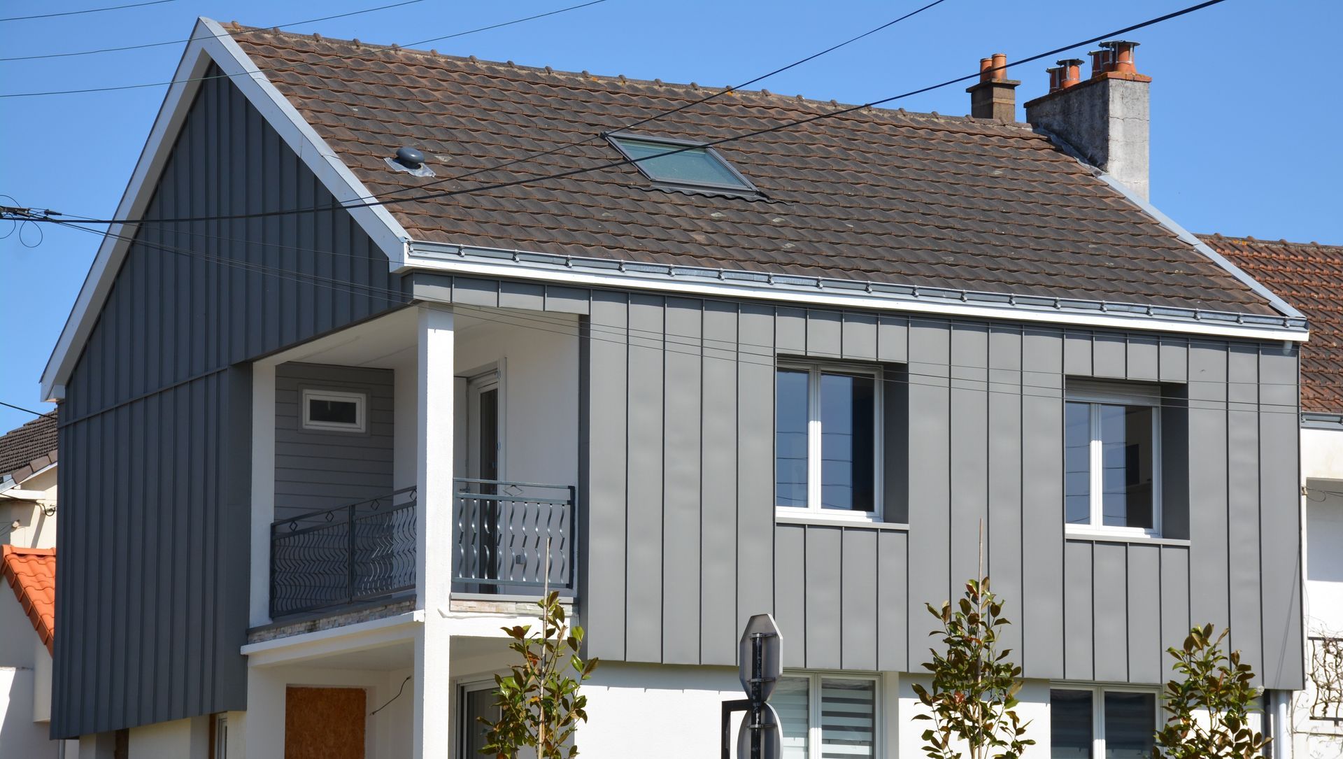 Maison moderne à deux étages avec bardage vertical gris, boiseries blanches et balcon.