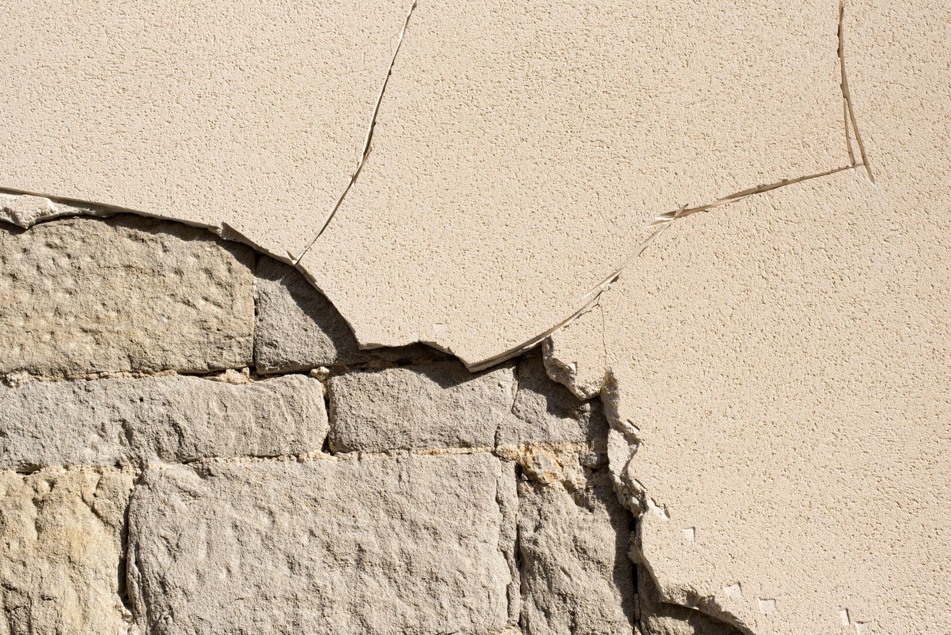 Gros plan sur un mur dont le stuc s'effrite, révélant les briques de pierre sous-jacentes.
