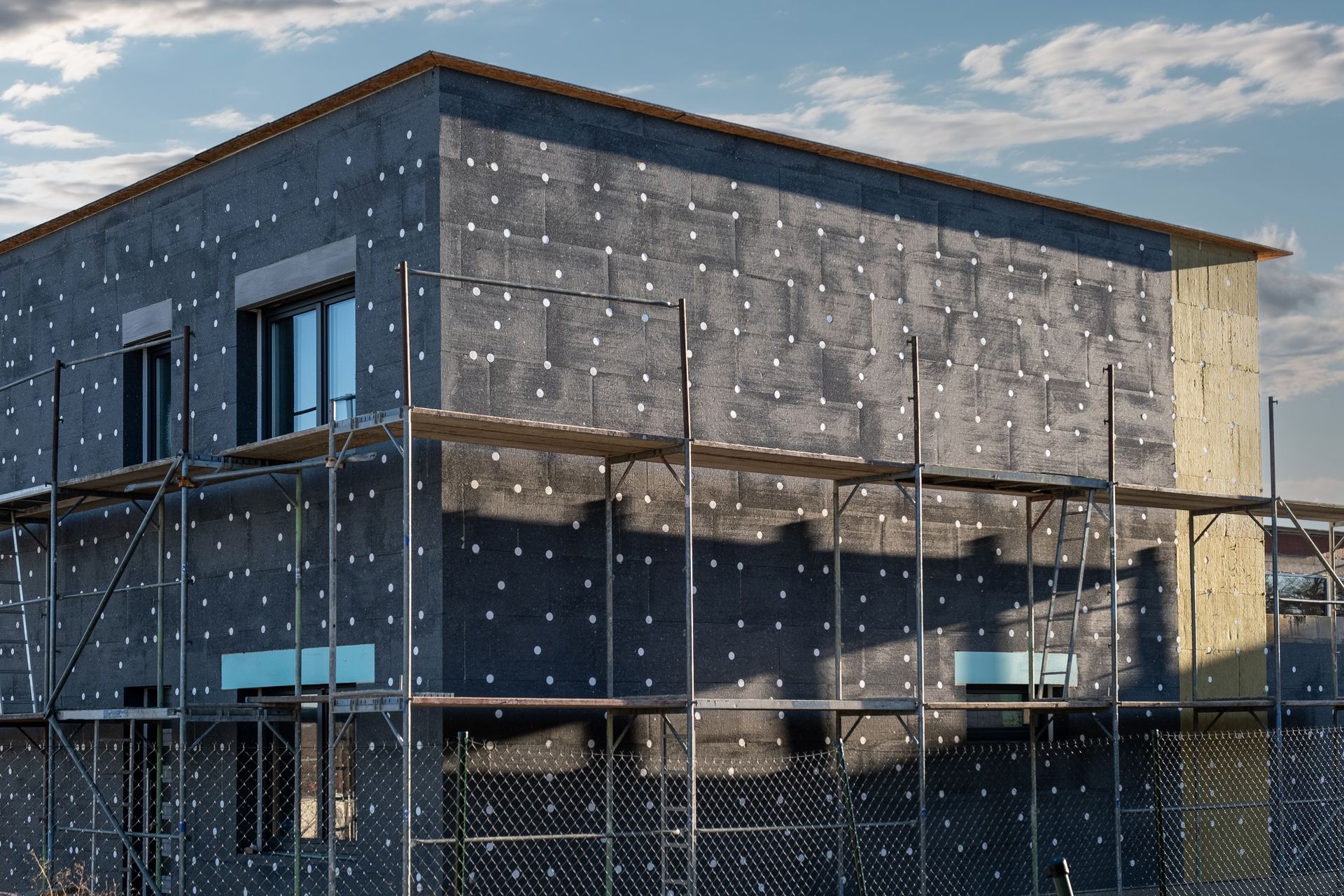 Bâtiment en construction ; extérieur gris, échafaudages, ciel bleu.
