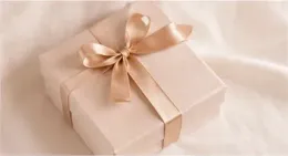 Caja de regalo color crema con un lazo de cinta de satén sobre un fondo beige suave