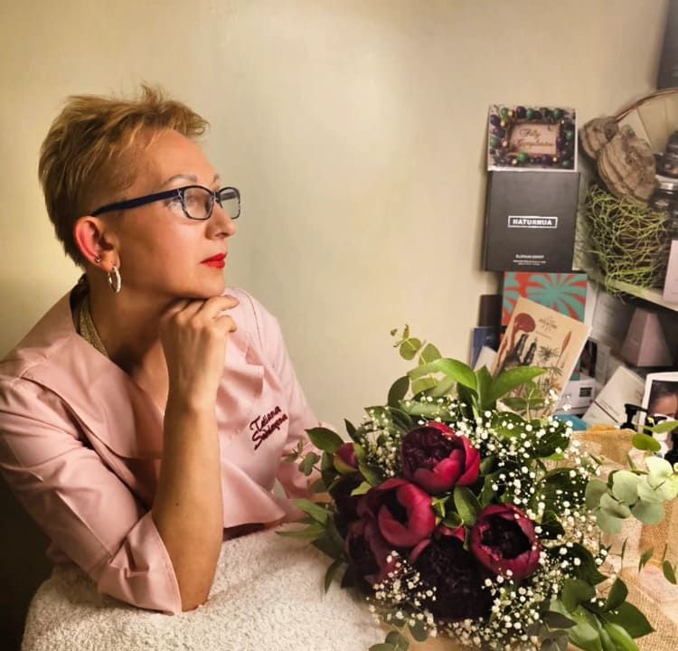 Una mujer con uniforme médico rosa contempla un ramo de flores rojas y blancas sobre una mesa