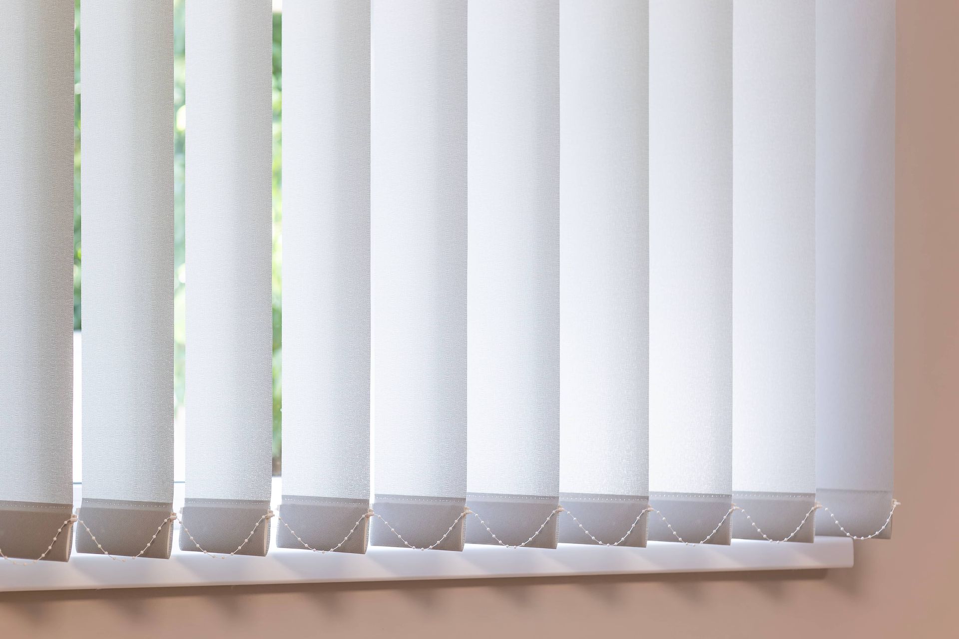 Stores verticaux blancs dans une fenêtre avec un mur beige.