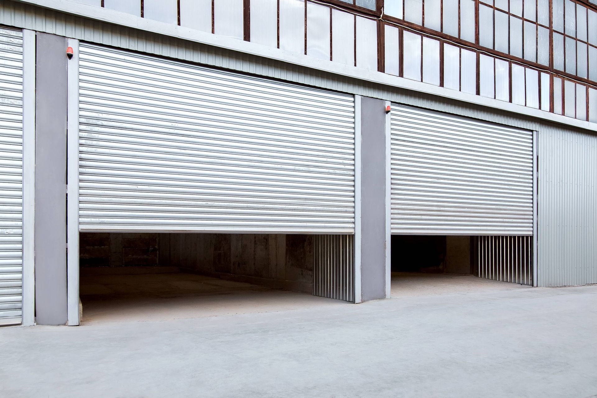 Deux portes sectionnelles argentées ouvertes sur un bâtiment commercial, révélant un intérieur sombre.