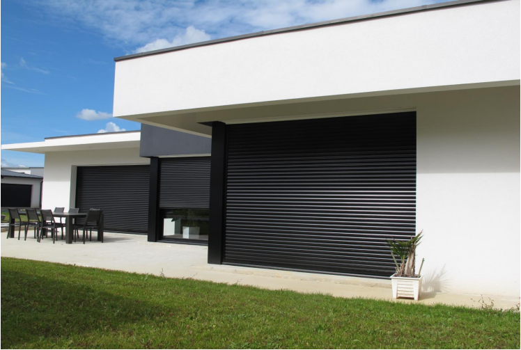 Maison blanche moderne avec de grands volets noirs, pelouse et ciel bleu.