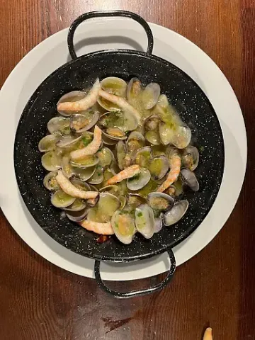 Una sartén llena de almejas y camarones en un plato blanco sobre una mesa de madera.