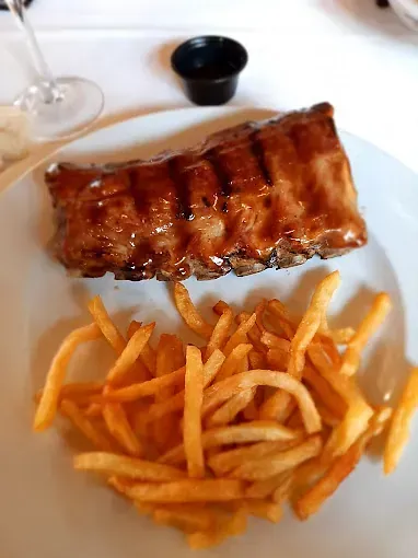 Un plato de comida con costillas y papas fritas en una mesa.