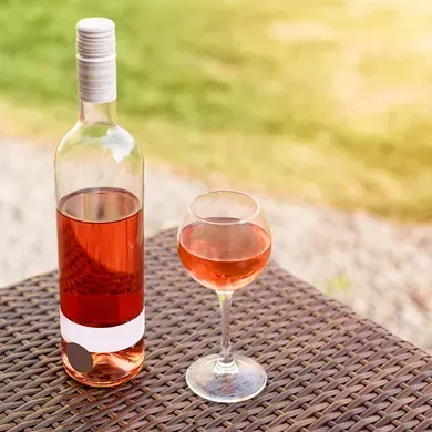 Una botella de vino rosado y una copa de vino están sobre una mesa de mimbre.