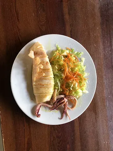 Un plato blanco cubierto con un calamar y una ensalada sobre una mesa de madera.