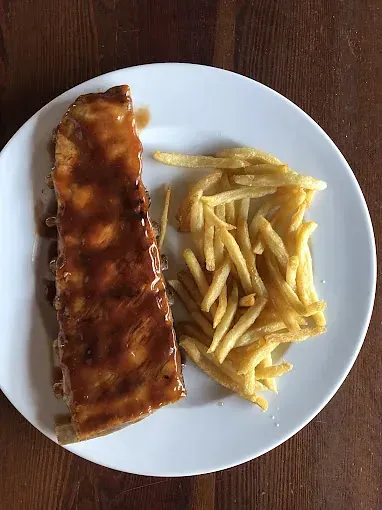 Un plato blanco cubierto con costillas y papas fritas sobre una mesa de madera.
