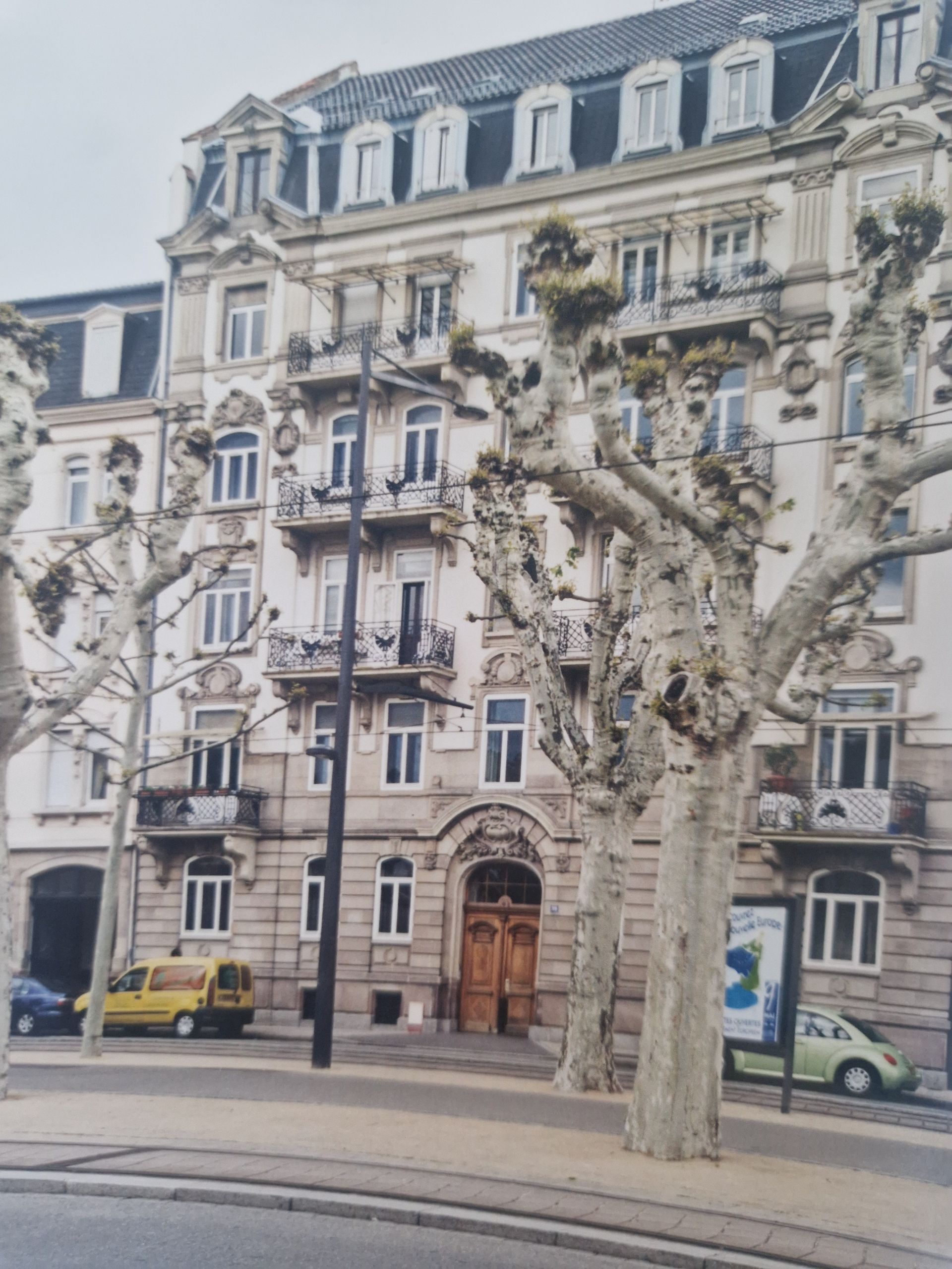 Un immeuble d'appartements européen orné, à plusieurs étages, avec des détails en pierre, des lucarnes et des arbres taillés à l'avant.