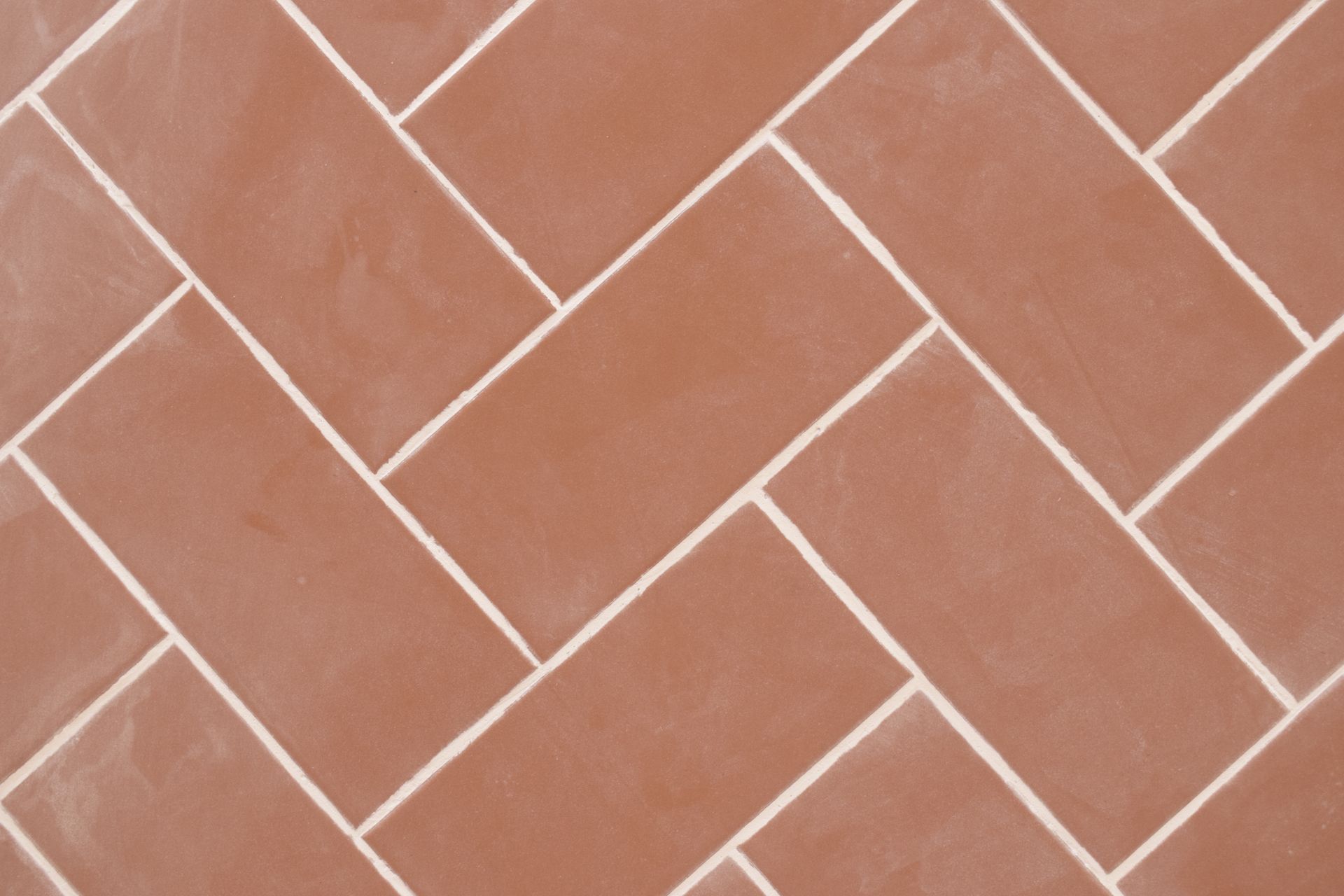 Carreaux rectangulaires brun rougeâtre disposés en motif à chevrons classique avec des joints blancs.