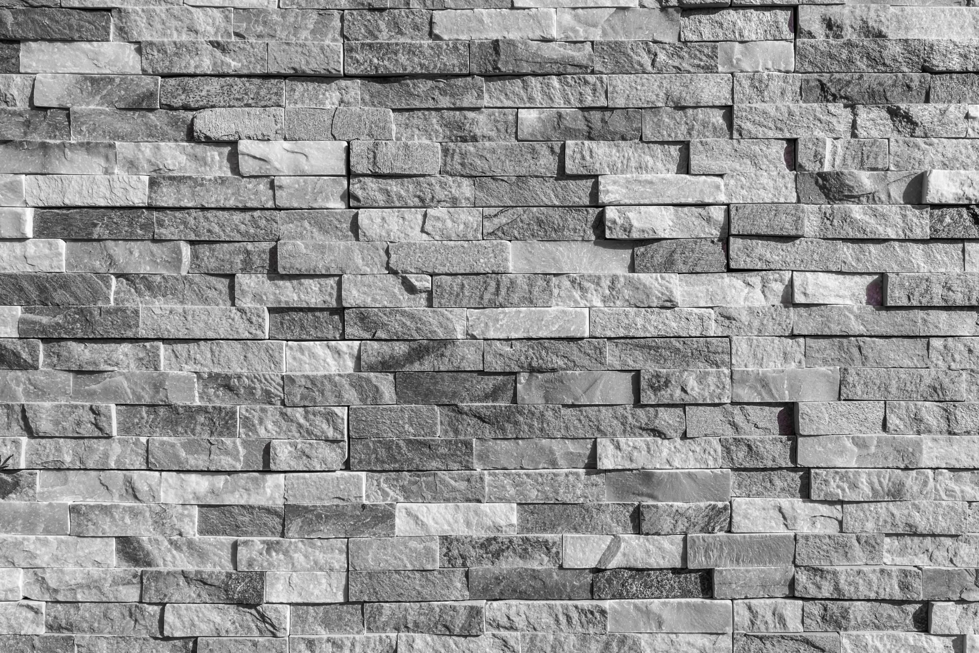 Une texture de briques de pierre naturelle grise empilées, de tailles et de nuances variées, créant un motif mural rustique et stratifié.