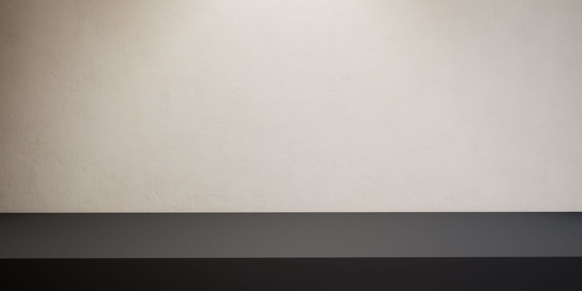 Un mur texturé, de couleur beige clair neutre, surplombe une surface horizontale lisse, gris foncé, éclairée par le haut.