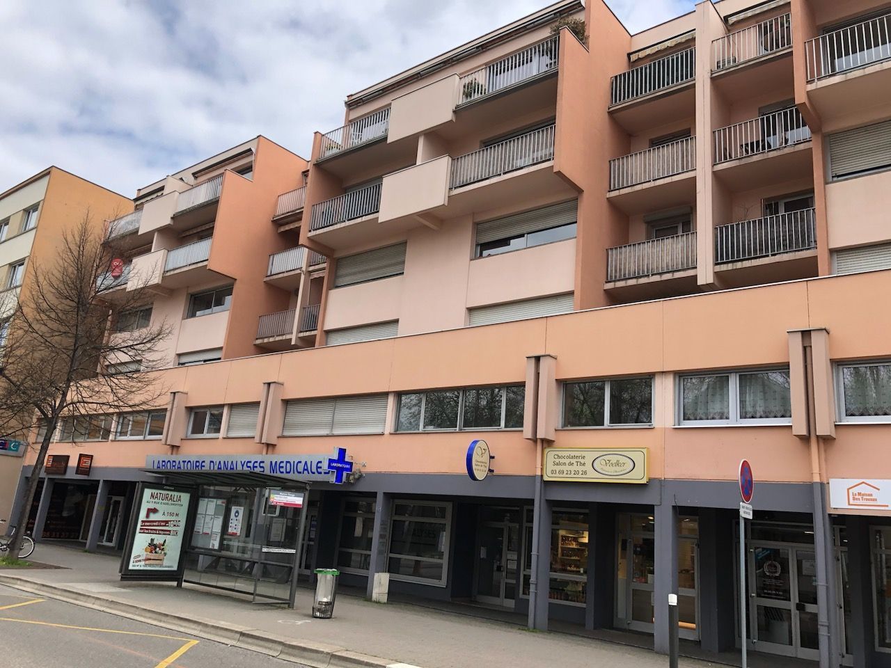 Un immeuble d'appartements de quatre étages, de couleur pêche, avec des commerces et une pharmacie au rez-de-chaussée.