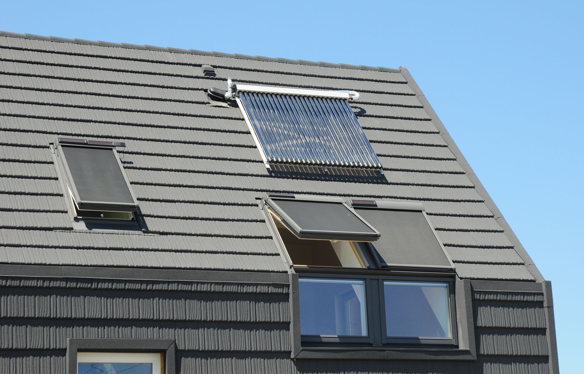 Toiture grise avec chauffe-eau solaire et VELUX avec stores extérieurs.