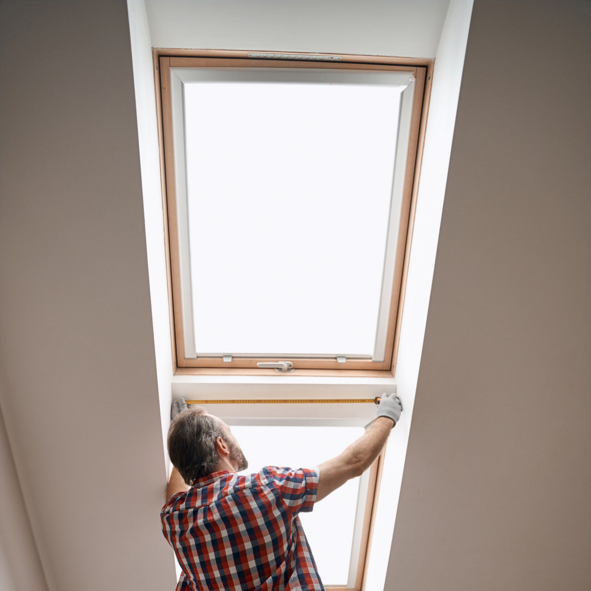 Personne ajustant une lucarne dans une pièce aux murs blancs.