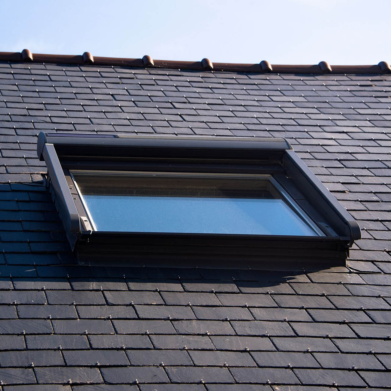 Velux sur un toit en ardoise gris foncé.