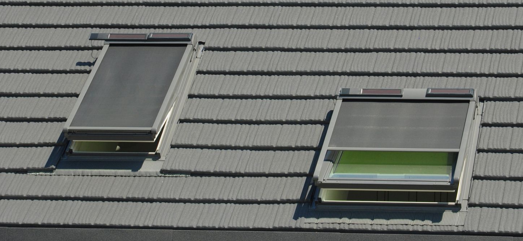Deux VELUX avec stores sur un toit en ardoises.