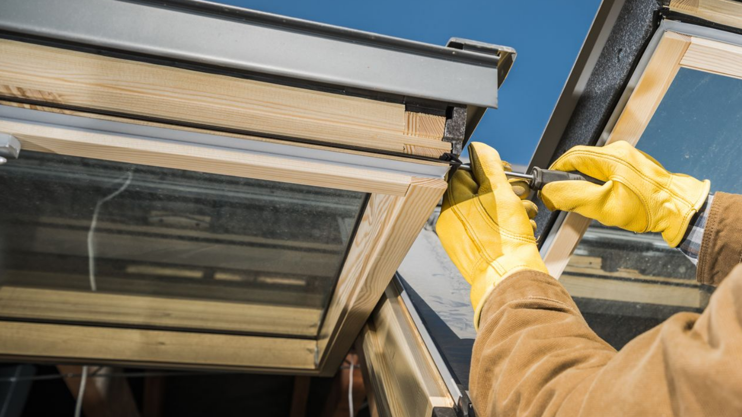 Une personne portant des gants jaunes utilisant un outil sur une fenêtre de toit.