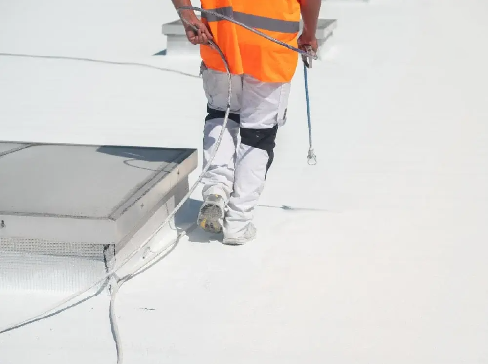 Un homme en veste orange applique du Cool Roof sur un toit