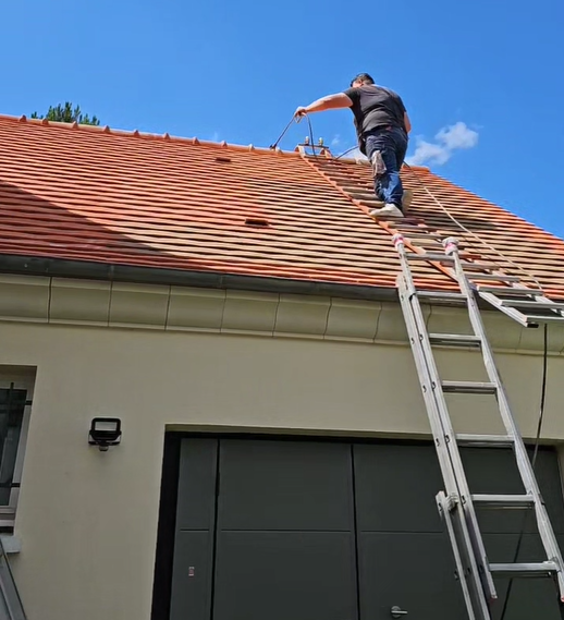 Un artisan sur une échelle effectue du nettoyage de toiture