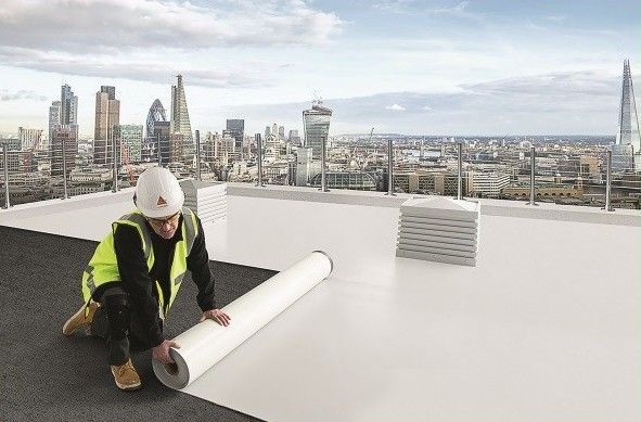 Un homme sur un toit plat installe une membrane d'étanchéité