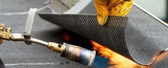 Un artisan applique de la membrane sur un toit plat